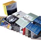 Ein geöffnetes Buch mit Bildern, daneben eine gelbe Schachtel und mehrere bunte Umschläge in Fächerform ausgelegt.