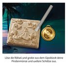 Auf einer Küstenlandschaft liegt ein Gipsblock mit Piratenmotiven, daneben eine Piratenmünze und ein Grabwerkzeug.