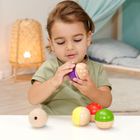 Ein Kind spielt mit bunten, halbkugelartigen Holzspielzeugen an einem Tisch, im Hintergrund ein warmes Licht und ein Bett.