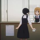 Zwei Mädchen in Schuluniform, eines mit schwarzem Haar, das andere mit blondem Haar, stehen in einem Klassenzimmer.