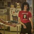 Zwei Personen in einem Raum. Eine trägt ein rotes T-Shirt mit "MAGIC DIRT" und "VIVA LA DIRT" sowie einem Porträt.