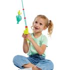 Ein Kind in grüner Kleidung hält eine bunte Spielzeug-Angel, mit einem grünen Fisch daran, in der Hand.