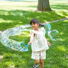 Ein Kind spielt draußen mit Seifenblasen in einem grünen Park. Das Kind trägt helle Kleidung und wirkt fröhlich.