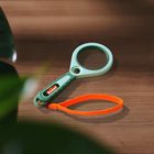 Text "Scout" auf einem Etikett. Eine grün-blaue Lupe mit orangener Schlaufe liegt auf Holzuntergrund. Links Pflanzen sichtbar.