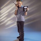 Ein Junge in Blau spricht in ein Funkgerät und zeigt einen Polizei-Ausweis mit Abzeichen. Lächelt freudig.