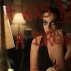 "IT WAS NOT A DREAM" steht in roter Schrift auf einem Spiegel. Eine Frau schminkt sich die Augen, eine Lampe scheint.