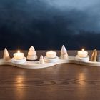 Kleine Holzlandschaft mit Kerzenhaltern in Baum- und Hausformen auf Holztisch, Kerzen brennen sanft im Dunkeln.