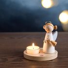 Der Text "HABA" ist auf einer Holzplatte zu sehen. Daneben steht eine Holzfigur eines Engels mit einem Teelicht vor dunklem Hintergrund.