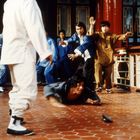 In einem asiatischen Tempel sieht man eine Gruppe Männer in Kampfposen. Einer liegt am Boden, umgeben von roten Säulen.