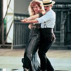Ein Tanzpaar in eleganter Kleidung tanzt auf einem schwarz-weiß karierten Boden. Sie wirken konzentriert und harmonisch.