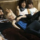 Harley-Davidson, Loveland. Vier Menschen entspannt auf einem Bett, ein Mann zeigt das Peace-Zeichen hinter einer Frau.