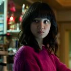 Eine Frau in einem Laden, trägt einen pinken Pullover und schaut zur Seite. Im Hintergrund sind Regale und Lichter.