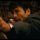 Ein Mann zielt konzentriert mit einem Bogen, der Hintergrund ist dunkel und holzartig.