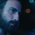 Ein Mann mit Bart blickt nachdenklich aus einem Fenster in bläulichem Licht, Bokeh-Lichtpunkte im Hintergrund.