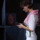 Eine Person in rosa-weißem Outfit hält etwas in der Hand, umgeben von Regalen mit rosafarbenen Masken.