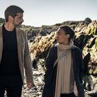 Ein Mann und eine Frau spazieren auf einem felsigen Strand. Sie unterhalten sich und tragen Herbstkleidung.