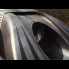 Ein futuristischer Zug aus grauem Metall mit aerodynamischem Design und geschwungenen Linien, der sich schnell bewegt.