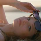 Keine erkennbaren Texte, Frau liegt entspannt auf einer Yacht, hält Sonnenbrille, Hintergrund zeigt Wasser und Sonnenuntergang.
