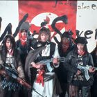 Text: "Jacta alea est" und "Wild Seven". Sieben Personen in winterlicher Kleidung, bewaffnet, vor Fahne.