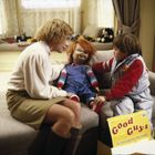 Eine Frau und ein Junge sitzen mit einer Puppe auf einem Sofa. Ein gelber Karton mit der Aufschrift "Good Guys" liegt daneben.