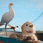 Illustration: Ein lächelnder Welpe und ein weißer Vogel in einem Boot vor blauem Himmel und grüner Landschaft.