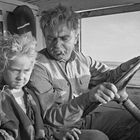 Ein älterer Mann fährt, schaut auf ein Kind neben ihm im Fahrzeug. Beide wirken nachdenklich.