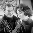 Ich kann die Personen nicht identifizieren, aber sie lächeln; ein Mann in Lederjacke, eine Frau mit dunklem Haar in Rollkragen.