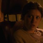 Eine junge Person sitzt in einem Auto, schaut aufmerksam nach rechts. Im Hintergrund ist ein Vorhang.