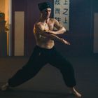 Ein Mann trainiert barfuß Martial Arts in einem Trainingsraum mit japanischen Schriftzeichen im Hintergrund.