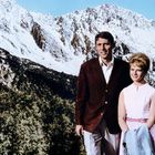 Keine Texte vorhanden. Ein Mann und eine Frau stehen vor schneebedeckten Bergen und grünen Bäumen.