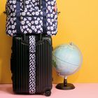 Eine schwarze Reisetasche mit Blumenmuster, darauf eine passende Stofftasche. Daneben ein Globus vor gelbem Hintergrund.