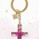 „Dein Wegbegleiter“. Ein goldener Schlüsselanhänger mit Stern und violettem Kreuz auf lila Hintergrund, „Coppenrath“.