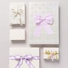 Fünf pastellfarbene Geschenkboxen mit Schleifen; lila, beiger, goldener und cremefarbener Dekoration; schlicht und elegant.