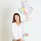 Person mit langem Haar hält einen bunten Ballon, trägt eine weiße Bluse, lächelt freundlich vor hellem Hintergrund.