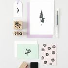 Verschiedene Karten mit floralen Stempeldrucken, Stempelblöcke und ein Stift auf einer weißen Fläche arrangiert.