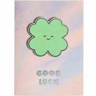 "Good Luck" in glitzernder Schrift, darunter ein grüner vierblättriger Kleeblatt mit lächelndem Gesicht vor pastellfarbenem Hintergrund.