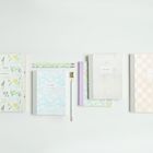 Text: "NOTEBOOK" mehrmals. Vier Notizbücher in Pastelltönen, Blumen- und geometrische Muster, Stifte und Klammer.