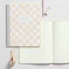 „Notebook“ auf kariertem Cover. Daneben ein offenes, leeres Buch, ein Bleistift mit Radiergummi und zwei Rollen Klebeband.