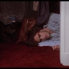 Eine Person liegt mit verletztem Kopf auf rotem Teppich vor einem geöffneten Kleiderschrank.