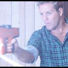 Ein Mann mit kariertem Hemd richtet ein Werkzeug, das Funken sprüht, auf eine Holzoberfläche.