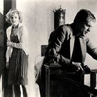 Text: "ROSE spoKE TAILOR". Eine Frau in gestreiftem Kleid schaut ängstlich, während ein Mann mit Waffe entspannt wirkt.