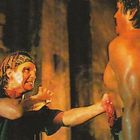 Zwei Männer, einer mit Bandana, der andere muskulös und blutend, stehen sich angespannt in einem dunklen Raum gegenüber.