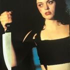 Oben steht: "Kerrang! Rose McGowan 'Devil In The Flesh'". Eine Frau hält ein großes Messer, mit ernstem Gesichtsausdruck.