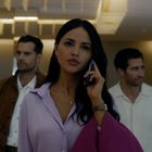 Eine Frau in lila Bluse telefoniert, gefolgt von zwei Männern in heller Kleidung in einem modernen Gebäude.