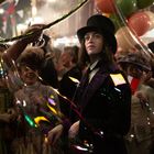 Ein Mann mit Zylinder schaut nachdenklich umgeben von fröhlichen Menschen auf einem bunten Fest mit Luftballons und Lichtern.