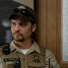 Uniformierter Mann mit Namensschild "G. Tooley", vor einer Zielscheibe und Karte. Polizist im Dienst.