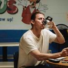 Texte: "never grow up!" und "LOST & FOUND". Ein Mann trinkt aus einer Kanne, sitzt an einem Tisch mit Gläsern und Fernbedienung.