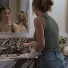 Ich erkenne keine Texte. Zwei Frauen sind im Badezimmer, eine putzt das Waschbecken, die andere spiegelt sich.