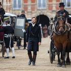 Ein Mann in schwarzem Anzug geht zwischen Pferdekutschen und Menschen in historischen Kostümen entlang.