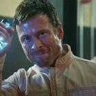 Ein Mann hält ein leuchtendes Objekt mit blauen Elementen in der Hand, wirkt konzentriert und entschlossen.